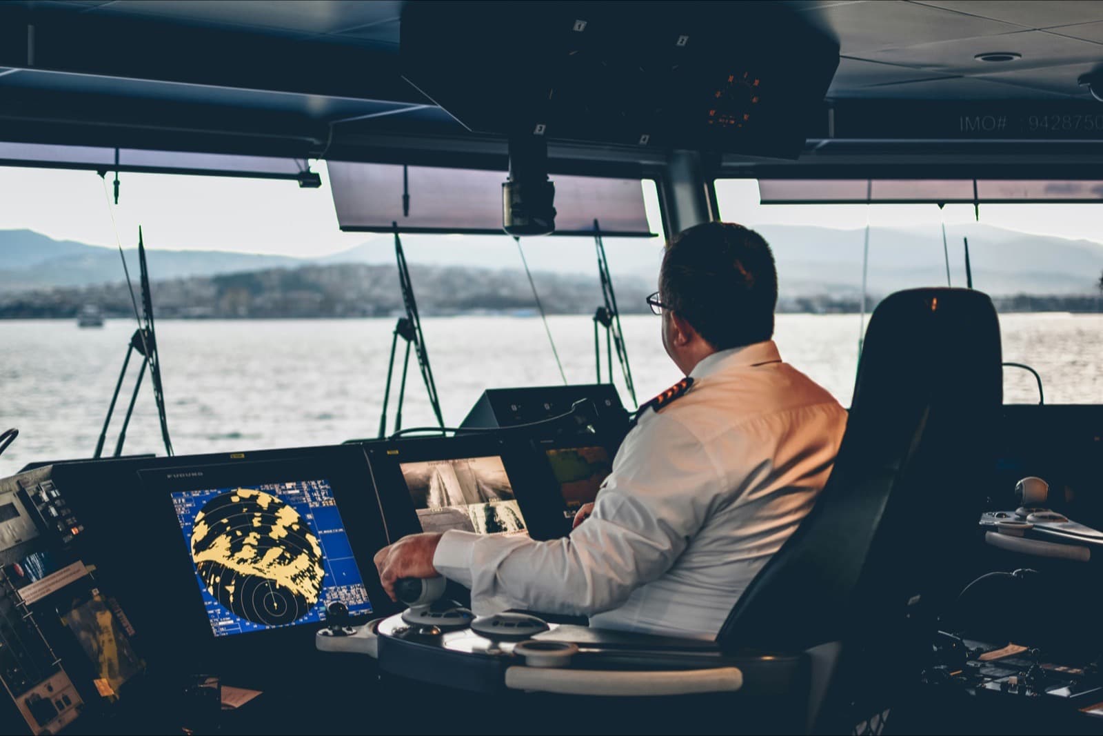 An officer at the bridge console of a merchant ship, radar and chart displays lit